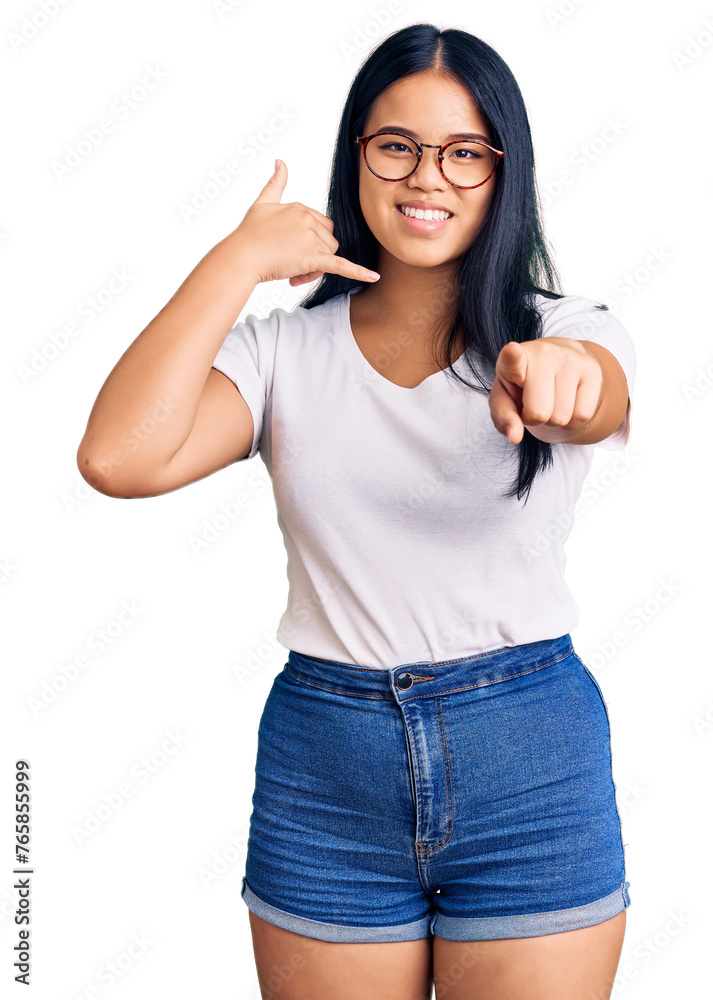 Young beautiful asian girl wearing casual clothes and glasses smiling doing talking on the telephone gesture and pointing to you. call me. Young beautiful asian girl wearing casual clothes and glasses smiling doing talking on the telephone gesture and pointing to you. call me.