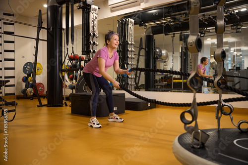 Mature european woman wearing sportswear doing sport exercise with ropes in gym