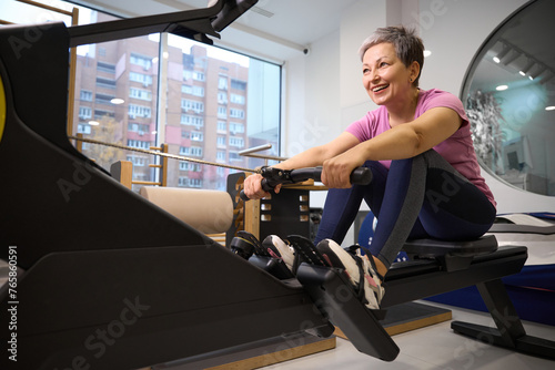 Adult smiling caucasian woman doing sport exercise for back on rowing trainer