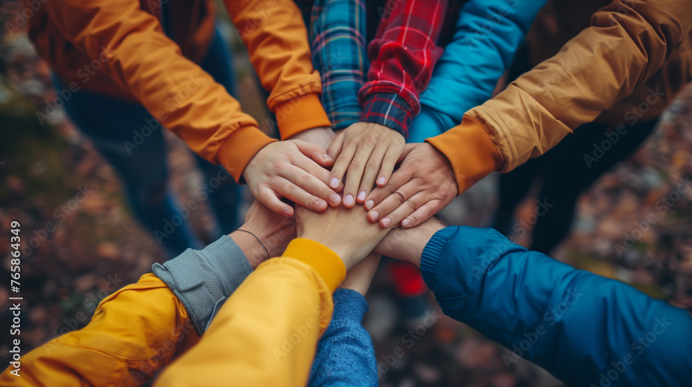 A diverse group of children's camp counselors stack hands together in a show of unity and teamwork, against a blurred autumn background. School activities in nature, environmental education.