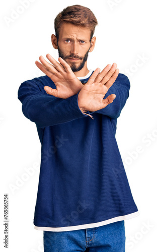 Handsome blond man with beard wearing casual sweater rejection expression crossing arms doing negative sign, angry face