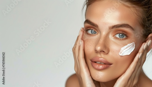 Giovane donna con la pelle radiosa che applica delicatamente una crema idratante sul viso. Trattamenti di bellezza e cura della pelle. photo