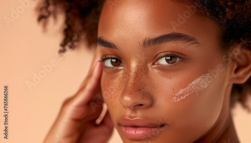 Giovane donna con la pelle radiosa che applica delicatamente una crema idratante sul viso. Trattamenti di bellezza e cura della pelle.