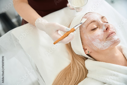 Cosmetologist applying moisturizing alginate mask on adult woman face