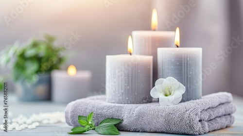  a set of three white candles sitting on top of a towel next to a white flower and a green plant.