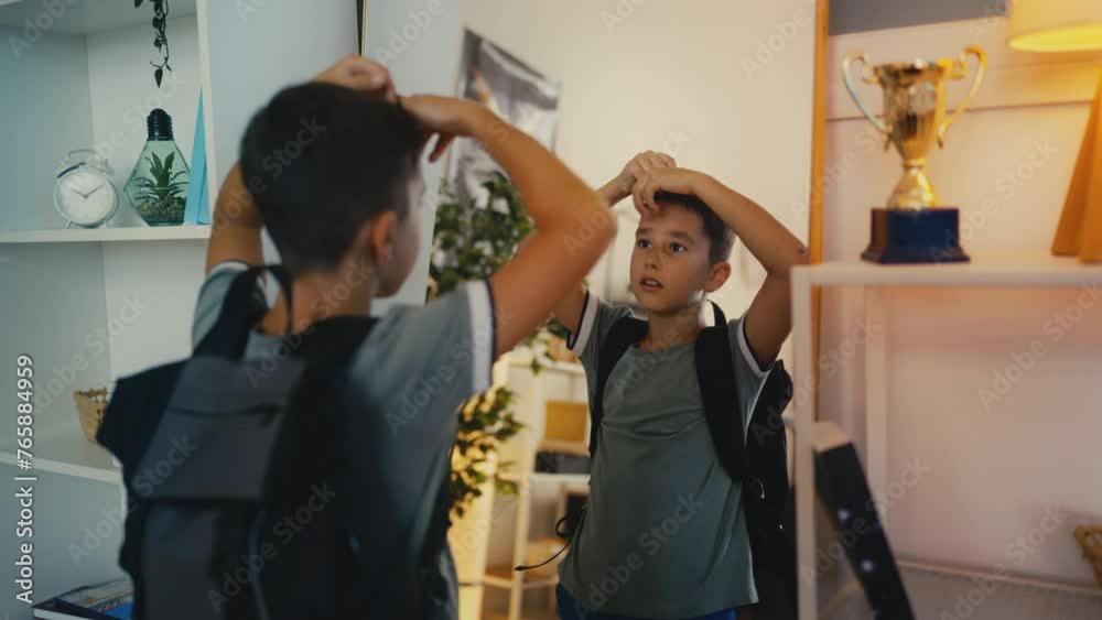 Boy with backpack adjusting hair in front of mirror, getting ready for school