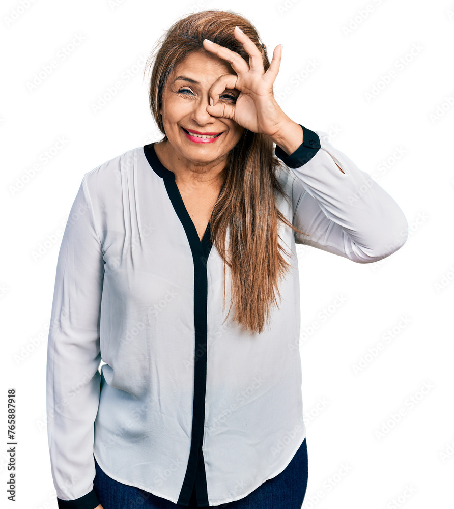 Middle age latin woman wearing business shirt doing ok gesture with hand smiling, eye looking through fingers with happy face. Middle age latin woman wearing business shirt doing ok gesture with hand smiling, eye looking through fingers with happy face.