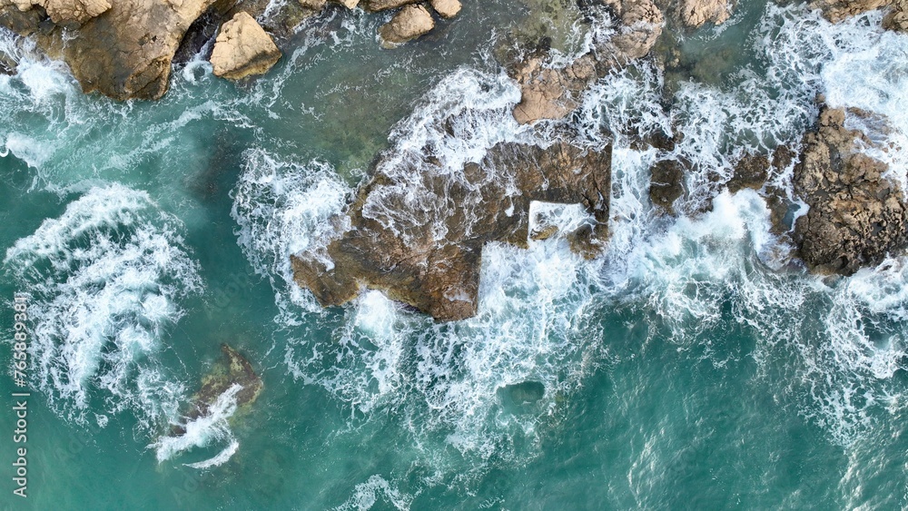 The colorful waters of the ocean swirl around the rocky and beautiful coastline. Sea waves passing over the rocks.