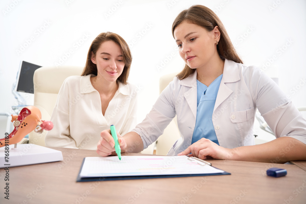 Gynecologist showing to young smiling woman her examining results in clinic Gynecologist showing to young smiling woman her examining results in clinic