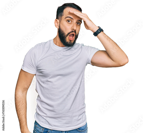 Young man with beard wearing casual white t shirt surprised with hand on head for mistake, remember error. forgot, bad memory concept.
