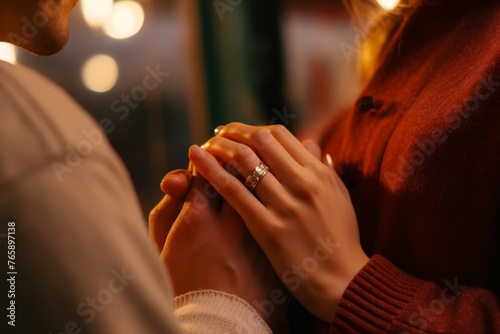 
Close-up of a man's hand presenting an engagement ring, with his elated girlfriend softly blurred in the background. photo