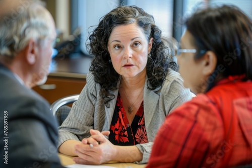 A woman sits at a table talking to two other people during a conflict resolution meeting, discussing and addressing issues