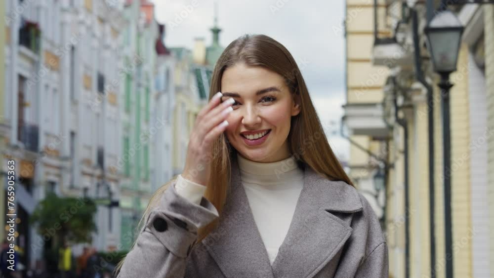 Joyful young woman with beaming smile poses on urban street, wearing chic coat and turtleneck, with historic city architecture on background Joyful young woman with beaming smile poses on urban street, wearing chic coat and turtleneck, with historic city architecture on background