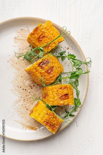 Top view of half plate with grilled fried slices of yellow corn or maize decorated with fresh pea microgreens with sauce served on white wooden table prepared for healthy vegetarian lunch appetizer