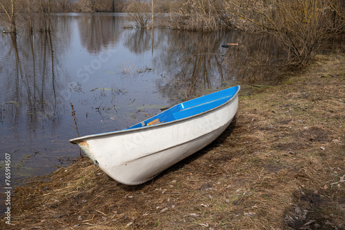 An empty boat on the shore of the overflowing floodplain of the river in spring.