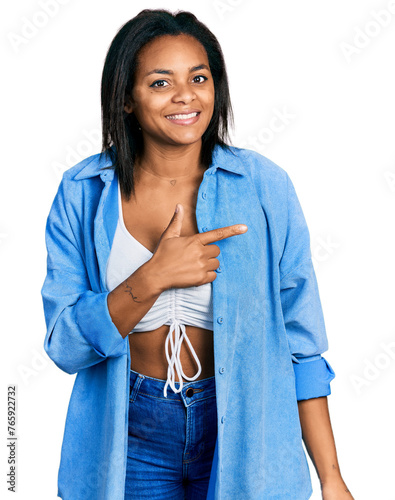 Beautiful hispanic woman wearing casual denim jacket cheerful with a smile of face pointing with hand and finger up to the side with happy and natural expression on face