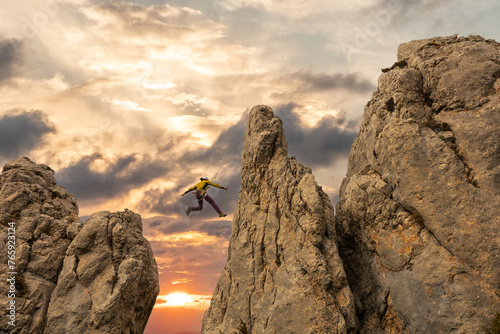 A man is jumping off a cliff with a green rope. Concept of adventure and excitement, as the man is taking a risk by jumping off a high point, In orange sunset.