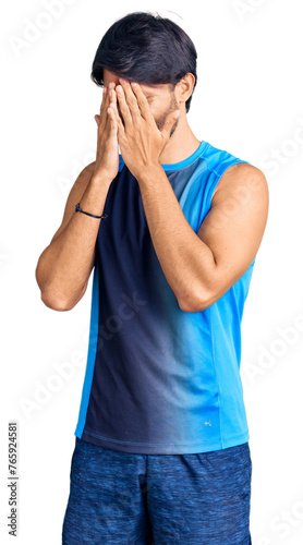 Handsome hispanic man wearing sportswear with sad expression covering face with hands while crying. depression concept.
