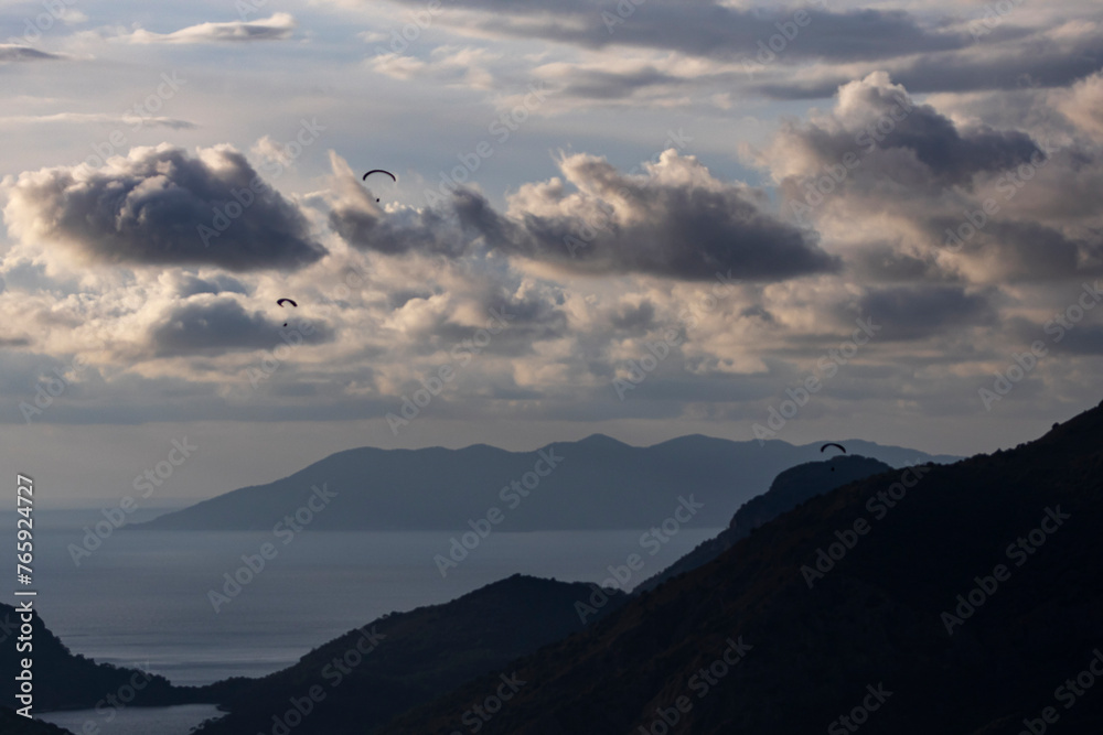Shot in Ölüdeniz with mountains in the background
 photo of parachutists flying in a row, one after another, with clouds, sea and sky