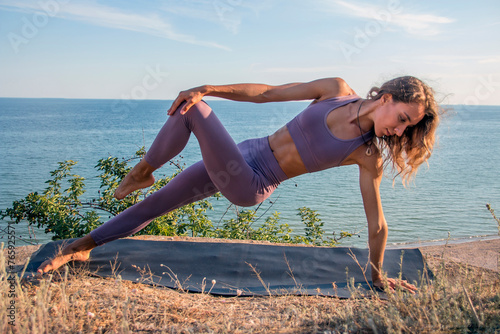 Beautiful girl - yoga in Vasishthasana pose against the backdrop of the sea on a cliff photo