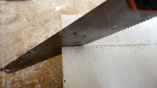 Close-up of a Caucasian man's hand cutting a block with a handsaw. A builder cuts an aerated concrete block according to the markings. Close-up of a hacksaw cutting a concrete block.