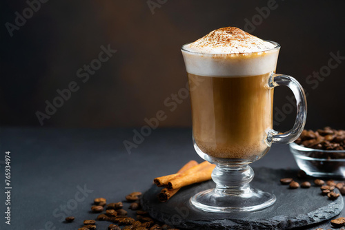 Cappuccino in a clear glass mug, with whipped cream on top, dusted with cinnamon, on a black background.