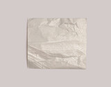 Torn empty crumbled texture silver nacre foil paper piece on neutral beige gray background.