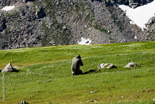 A man photographer in the green meadow photographing from afar, with his digital camera, an awake wild alpine marmot just out of the den in the Gran Paradiso National Park, Aosta Valley, Italy