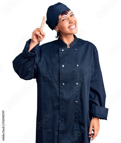 Young brunette woman with short hair wearing professional cook uniform pointing finger up with successful idea. exited and happy. number one.