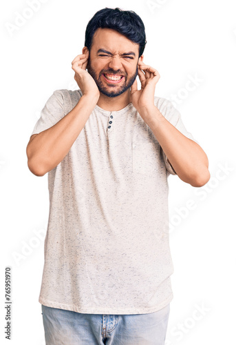 Young hispanic man wearing casual clothes covering ears with fingers with annoyed expression for the noise of loud music. deaf concept.