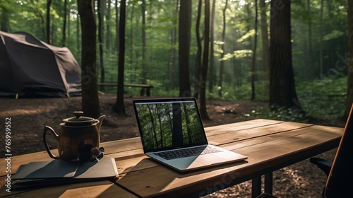 Laptop computer on wooden table in morning forest with aromatic cup of coffee. Remote office work outside ,  from anywhere, camping