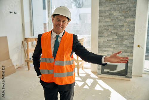 Happy foreman standing in room and invites someone to enter