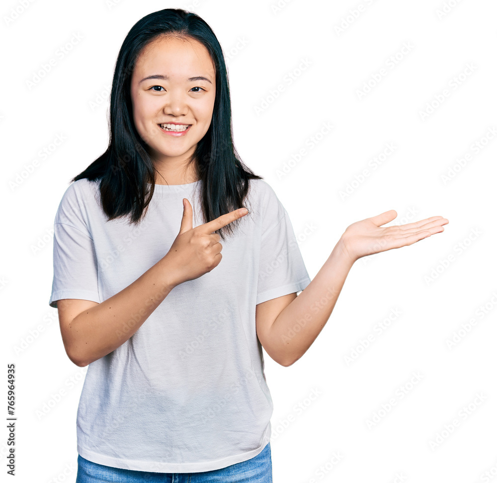 Young chinese woman wearing casual white t shirt amazed and smiling to the camera while presenting with hand and pointing with finger. Young chinese woman wearing casual white t shirt amazed and smiling to the camera while presenting with hand and pointing with finger.