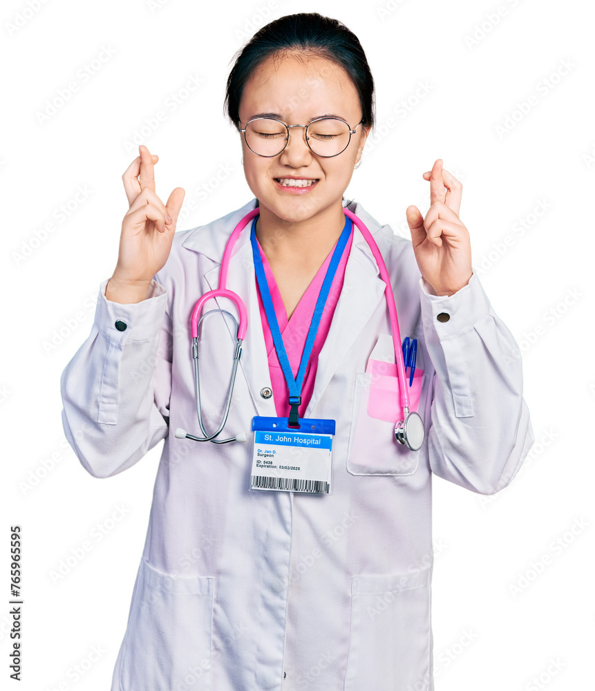Young chinese woman wearing doctor uniform and stethoscope gesturing finger crossed smiling with hope and eyes closed. luck and superstitious concept. Young chinese woman wearing doctor uniform and stethoscope gesturing finger crossed smiling with hope and eyes closed. luck and superstitious concept.