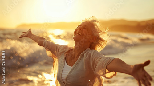 Happy mature woman dancing freely on the beach with her face beaming with laughter against the backdrop of crashing waves.