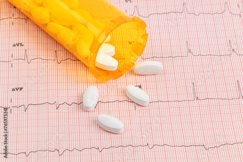 Anti cholesterol pills used for hypertension and heart disease treatment spilled out on an electrocardiogram (ECG) printout photo