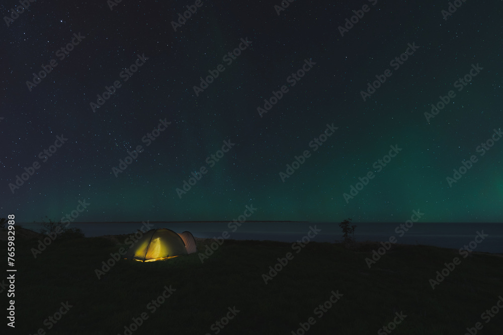 The tent stands on the seashore, the northern lights are on the horizon.