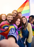 Vertical fun selfie LGBT group young friends celebrating gay pride day together holding rainbow flag. Homosexual people community smiling and taking portrait outdoor. Generation z positive relations.