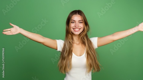  pretty young woman with hair bun, smiles pleasantly, dressed in casual outfit, keeps arms raised up, isolated over green background copy space