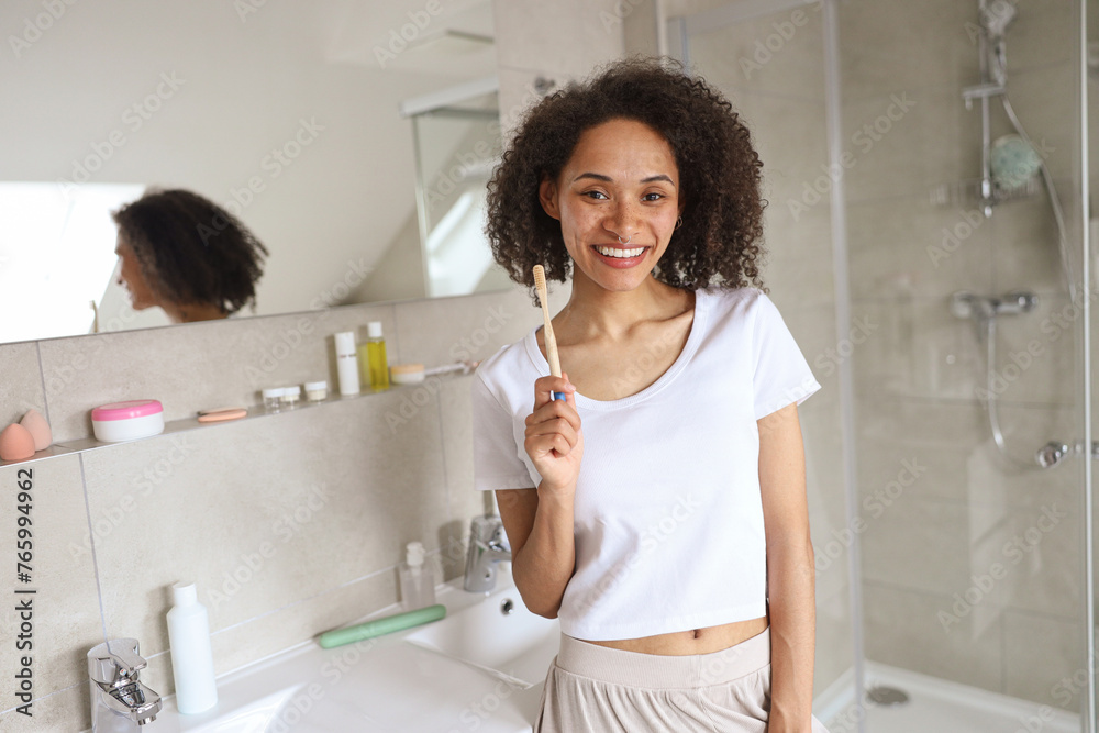 The woman is brushing her teeth in the bathroom, flashing a smile in the mirror