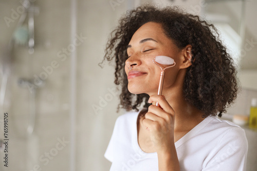 Black hair woman happily rolls rose quartz on face for a spa ritual