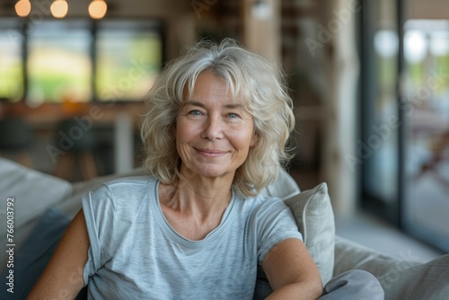 A woman with gray hair is sitting on a couch and smiling