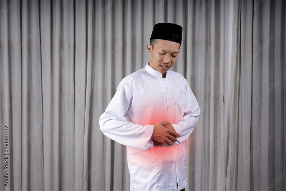 Muslim Asian man touching his stomach with in pain expression. Diseases of the gastrointestinal tract that often cause abdominal pain, such as appendicitis, enteritis Muslim Asian man touching his stomach with in pain expression. Diseases of the gastrointestinal tract that often cause abdominal pain, such as appendicitis, enteritis