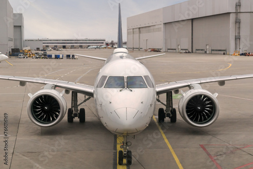Front view of a modern twinjet airliner sitting on the concrete tarmac with lane markings in a large airport