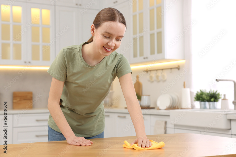 Woman with microfiber cloth cleaning wooden table in kitchen Woman with microfiber cloth cleaning wooden table in kitchen