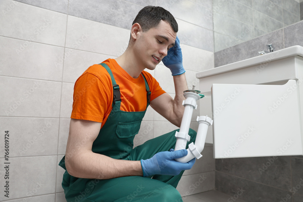 Thoughtful plumber wearing protective gloves repairing sink in bathroom Thoughtful plumber wearing protective gloves repairing sink in bathroom