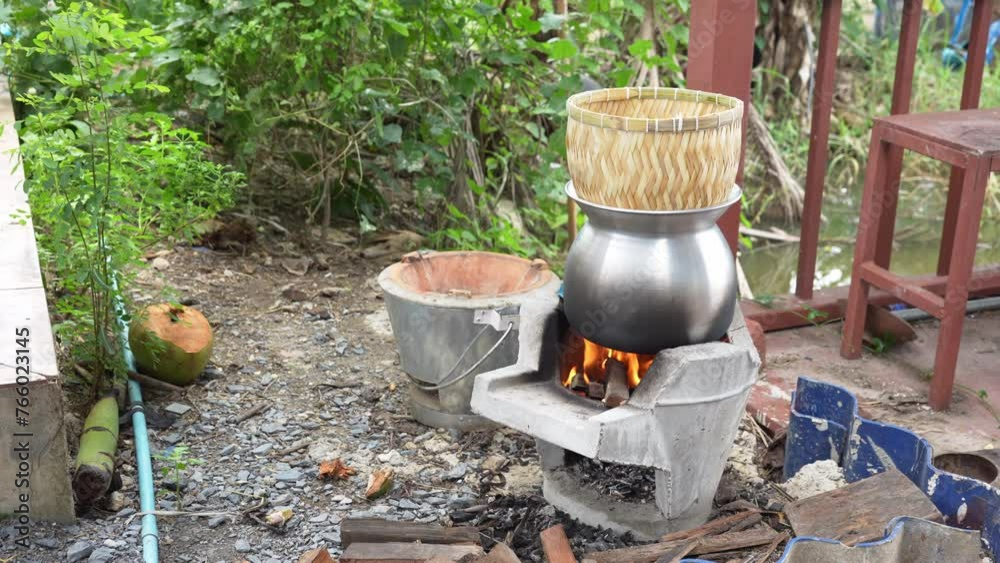 The smoke from the steamed sticky rice cooked in wicker bamboo steamer with laos aluminum steel pot on the charcoal stove in the agricultural garden house area. The smoke from the steamed sticky rice cooked in wicker bamboo steamer with laos aluminum steel pot on the charcoal stove in the agricultural garden house area.