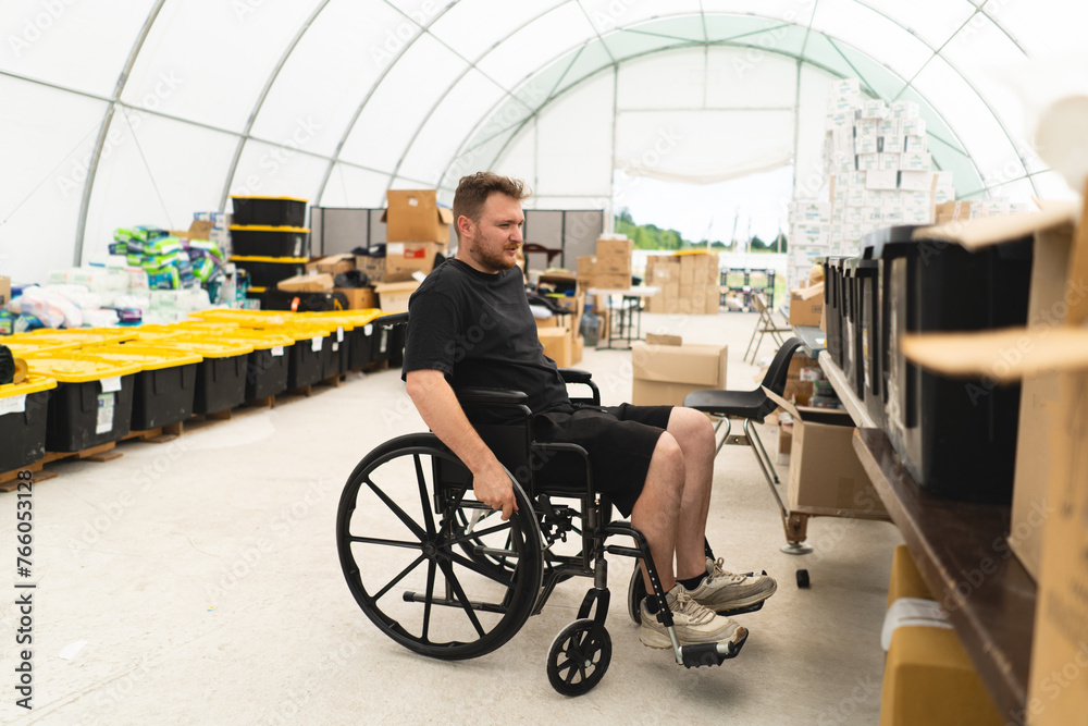 Obraz premium A veteran disabled man in a wheelchair helps in a humanitarian unit. Support of war victims. Humanitarian aid concept. Helping people