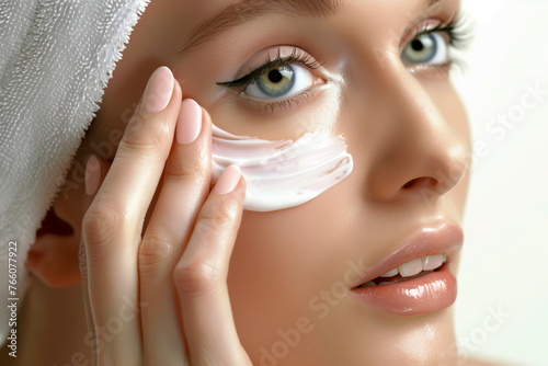 A woman is applying cream to her face. She has a smile on her face and her eyes are wide open