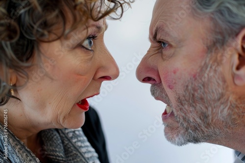 Mid-aged couple in the midst of an argument, isolated against a white studio background. Their faces are close, eyes locked in a confrontational gaze, mouths open as if caught mid-yell. photo